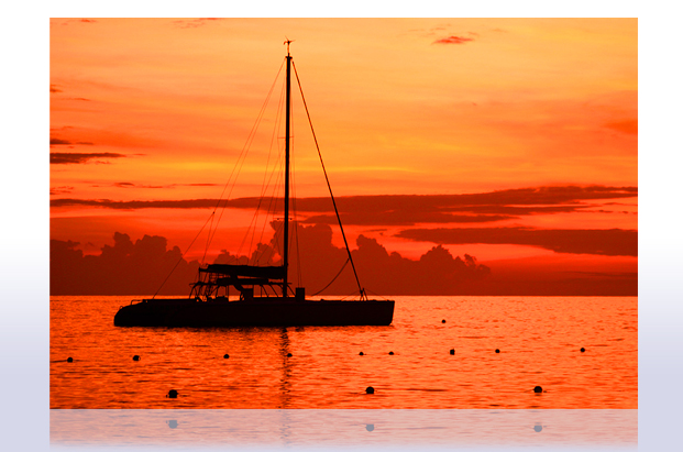 A sailboat silhouetted against an orange sunset, from Lloyd Watts’s photography collection